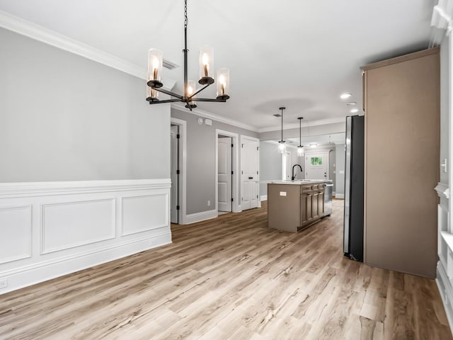 kitchen featuring a kitchen island with sink, sink, hanging light fixtures, a notable chandelier, and stainless steel refrigerator