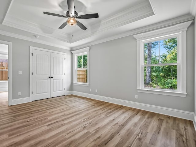 unfurnished bedroom featuring a raised ceiling, ceiling fan, crown molding, and light wood-type flooring