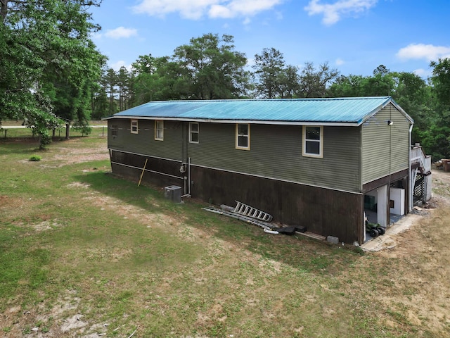 view of side of property with a lawn, central AC unit, and metal roof