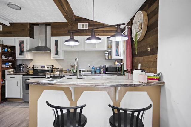 kitchen with wall chimney range hood, a breakfast bar area, visible vents, appliances with stainless steel finishes, and wood walls