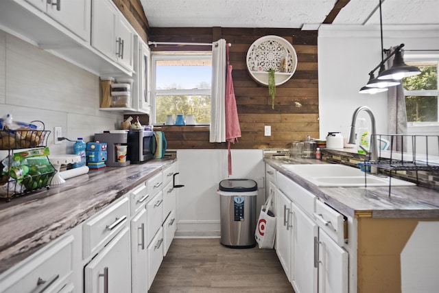 kitchen featuring decorative light fixtures, wood finished floors, a sink, white cabinets, and wooden walls