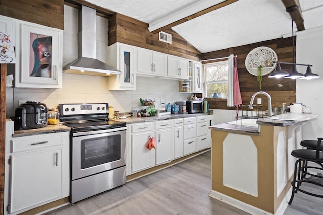 kitchen with visible vents, a peninsula, wall chimney range hood, vaulted ceiling with beams, and appliances with stainless steel finishes