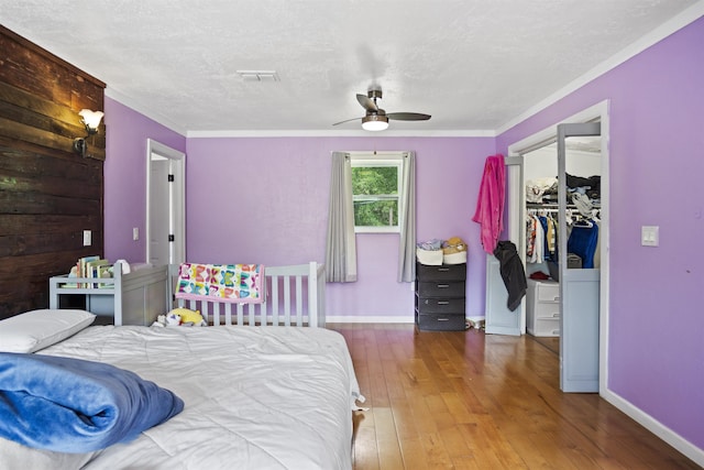 bedroom with a textured ceiling, hardwood / wood-style flooring, baseboards, a closet, and a spacious closet