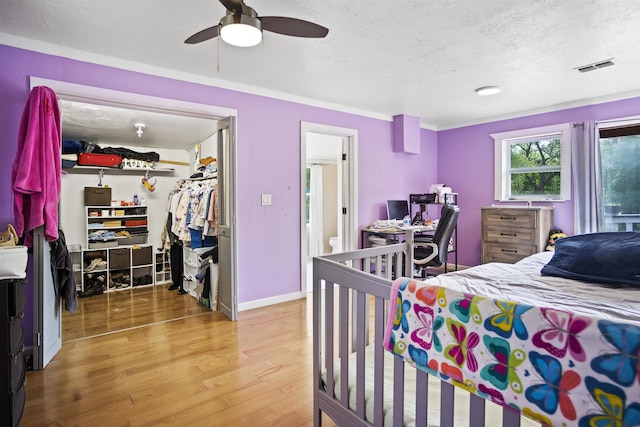 bedroom featuring a textured ceiling, a ceiling fan, wood finished floors, visible vents, and a closet