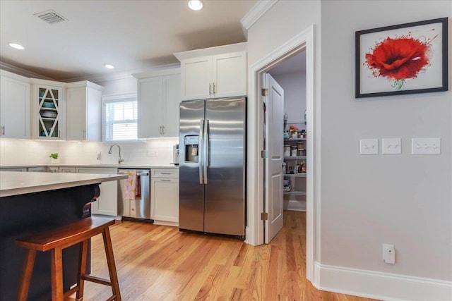 3837 Broadmore Ln, Tallahassee, FL 32308 - kitchen featuring appliances with stainless steel finishes, light countertops, white cabinetry, tasteful backsplash, and light wood finished floors