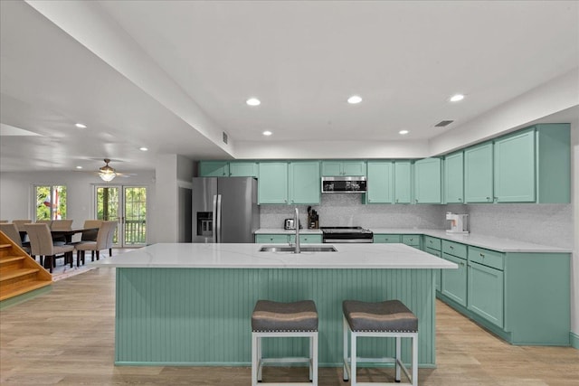 kitchen featuring stainless steel appliances, a kitchen island with sink, sink, and light hardwood / wood-style flooring