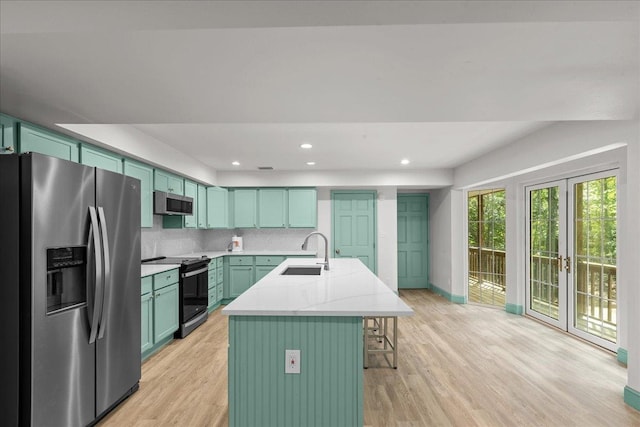 kitchen with a kitchen island with sink, sink, light wood-type flooring, and appliances with stainless steel finishes