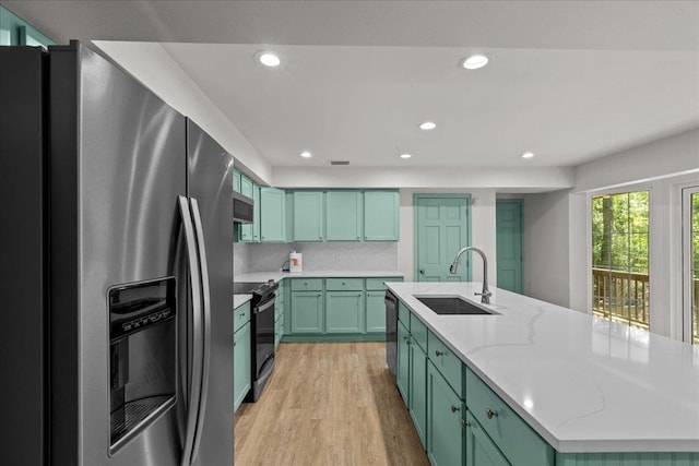 kitchen featuring sink, appliances with stainless steel finishes, a kitchen island with sink, light stone countertops, and light wood-type flooring