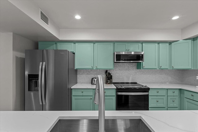 kitchen featuring stainless steel appliances, light stone countertops, green cabinets, and backsplash