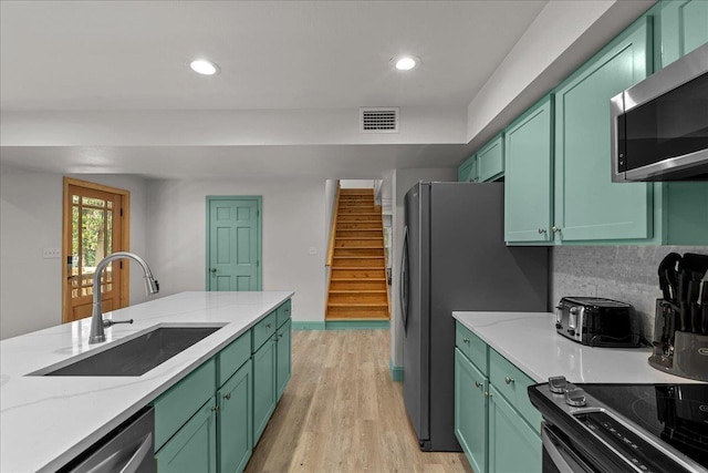 kitchen featuring stainless steel appliances, light stone countertops, sink, and green cabinets