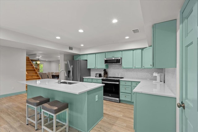 kitchen featuring sink, light hardwood / wood-style flooring, appliances with stainless steel finishes, an island with sink, and decorative backsplash