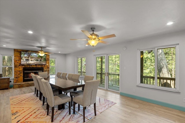 dining room with a stone fireplace, plenty of natural light, ceiling fan, and light hardwood / wood-style flooring