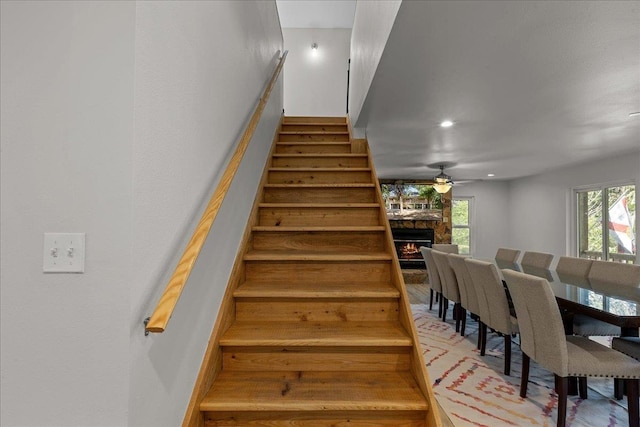 stairway featuring ceiling fan and a stone fireplace