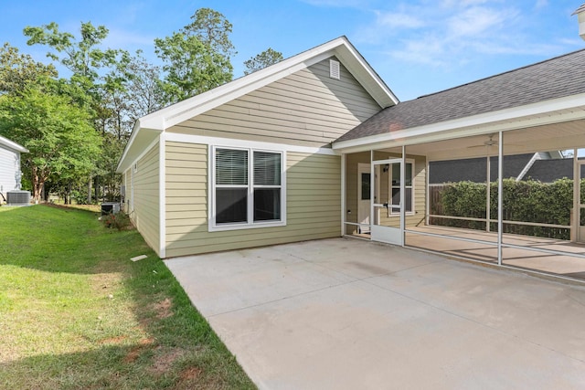 back of house with cooling unit, a sunroom, a shingled roof, a patio area, and a lawn