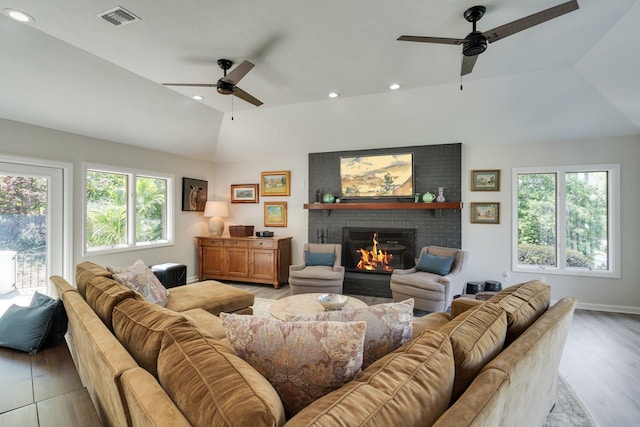 living area featuring ceiling fan, a brick fireplace, plenty of natural light, light wood-style flooring, and lofted ceiling