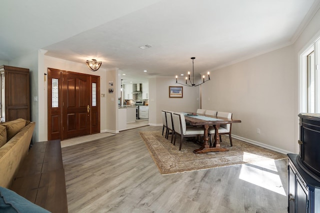 dining space with a chandelier, light wood finished floors, ornamental molding, and baseboards