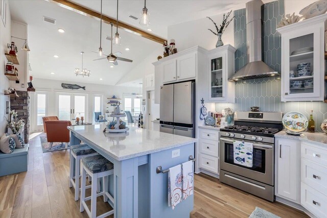 kitchen featuring wall chimney range hood, appliances with stainless steel finishes, tasteful backsplash, decorative light fixtures, and white cabinetry