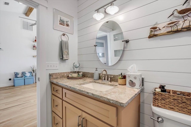 bathroom featuring vanity, wooden walls, toilet, beam ceiling, and wood-type flooring