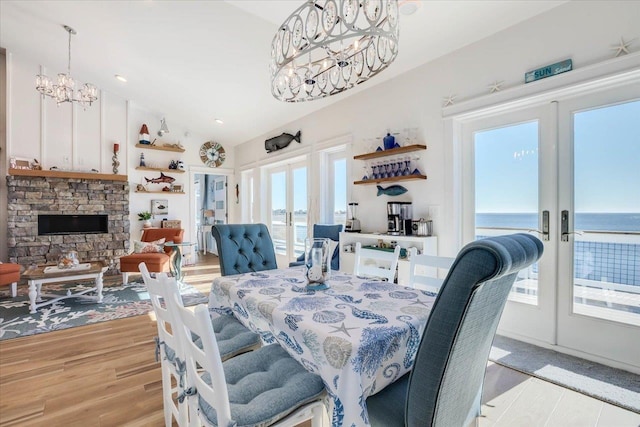 dining area with french doors, a water view, a stone fireplace, and light hardwood / wood-style floors