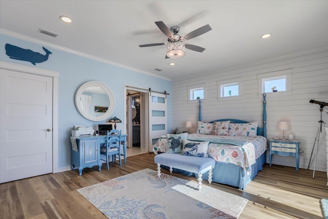 bedroom with a barn door, light hardwood / wood-style flooring, ceiling fan, and crown molding