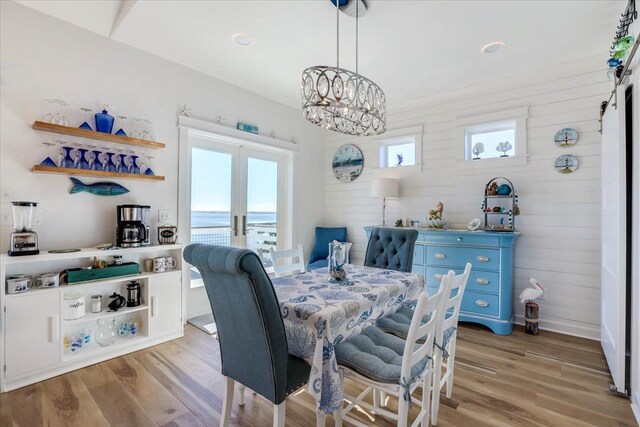 dining area with hardwood / wood-style floors, wood walls, french doors, a water view, and a chandelier