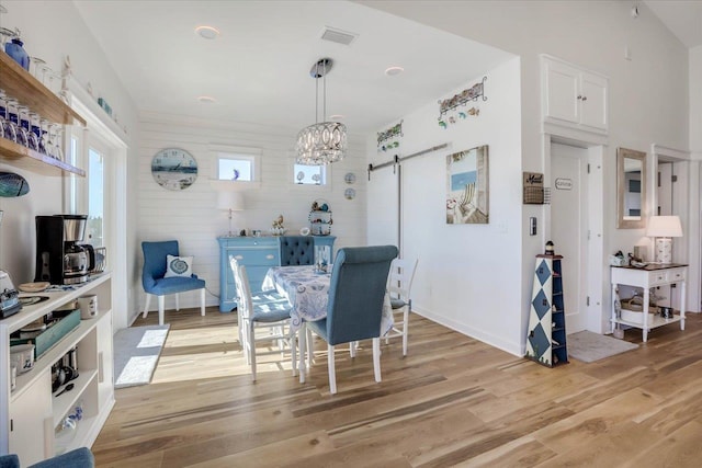 dining room featuring wood walls, a notable chandelier, a barn door, and light hardwood / wood-style flooring