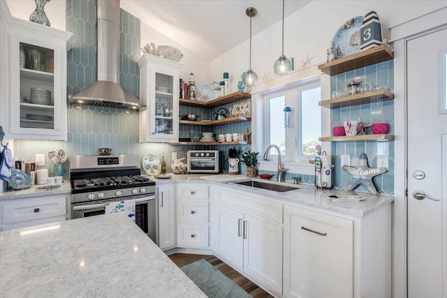 kitchen with light stone countertops, wall chimney exhaust hood, sink, stainless steel gas stove, and white cabinetry