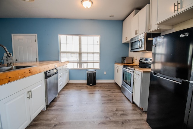 kitchen with stainless steel appliances, white cabinetry, sink, and light hardwood / wood-style flooring