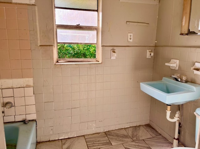 full bathroom featuring a bathing tub, tile walls, marble finish floor, and a sink