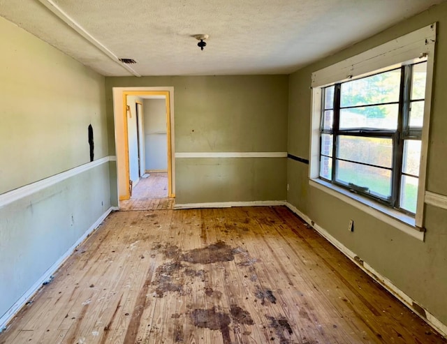 spare room featuring baseboards, a textured ceiling, wood-type flooring, and visible vents
