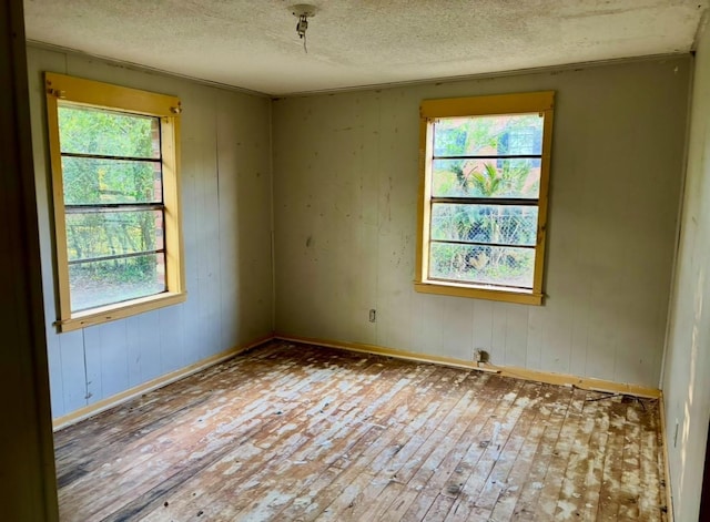 empty room with a textured ceiling, wooden walls, wood-type flooring, and baseboards