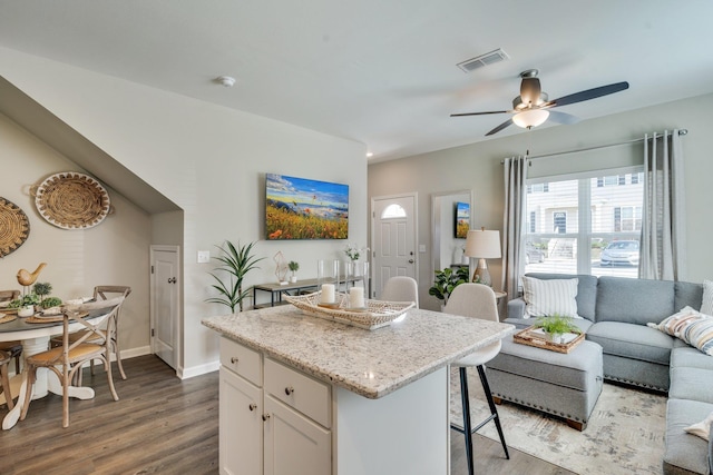 kitchen featuring dark wood-type flooring, white cabinetry, a kitchen island, ceiling fan, and light stone countertops