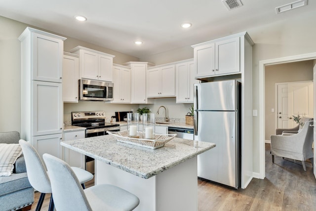 kitchen featuring white cabinetry, appliances with stainless steel finishes, a kitchen breakfast bar, and light stone counters