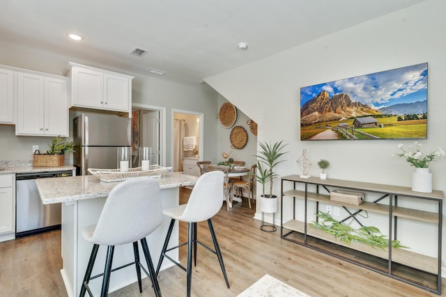 kitchen featuring a breakfast bar area, white cabinetry, a center island, stainless steel appliances, and light stone countertops