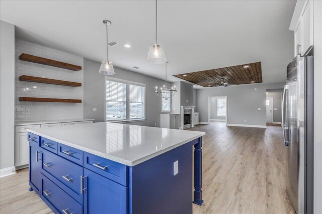 kitchen with blue cabinetry, light countertops, backsplash, freestanding refrigerator, and white cabinets