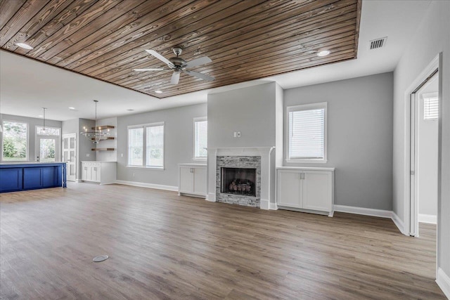 unfurnished living room with ceiling fan with notable chandelier, visible vents, a stone fireplace, and wood finished floors