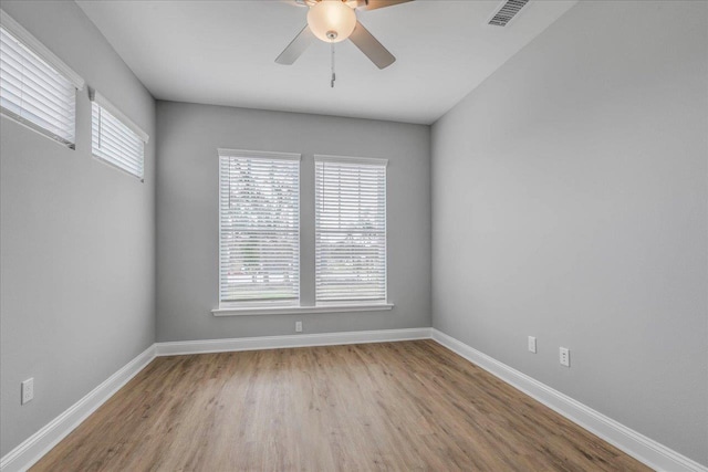 unfurnished room with plenty of natural light, wood finished floors, visible vents, and baseboards