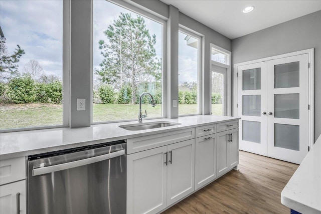 kitchen featuring dishwasher, wood finished floors, light countertops, a sink, and recessed lighting