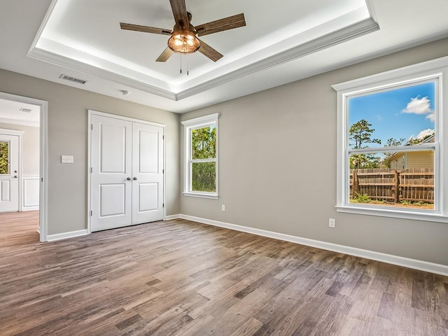 unfurnished bedroom with a closet, a tray ceiling, ceiling fan, and light hardwood / wood-style floors