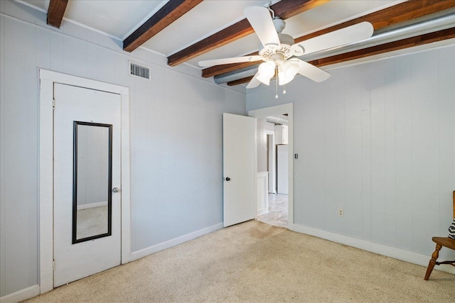 unfurnished bedroom with ceiling fan, beamed ceiling, wooden walls, and light colored carpet