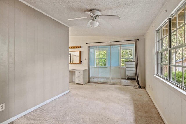 unfurnished room featuring built in desk, ceiling fan, a healthy amount of sunlight, and light carpet