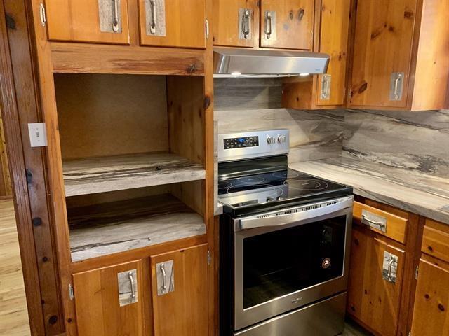 1915 Sunset Ln, Tallahassee, FL 32303 - kitchen featuring electric range, under cabinet range hood, brown cabinetry, light countertops, and decorative backsplash