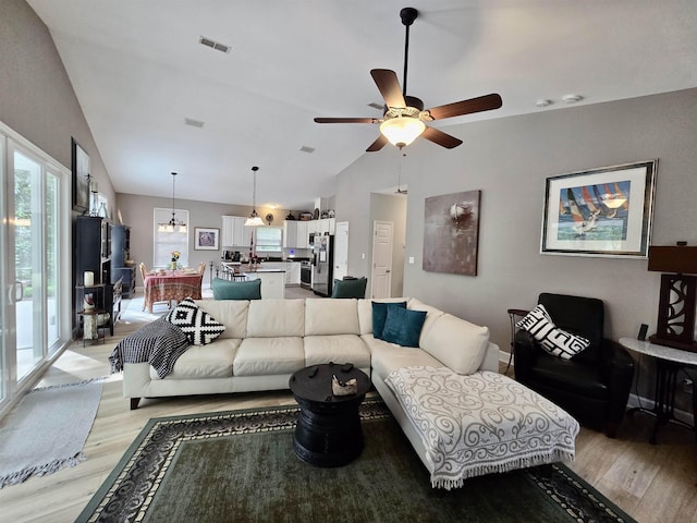 living area featuring ceiling fan, lofted ceiling, visible vents, and light wood-type flooring