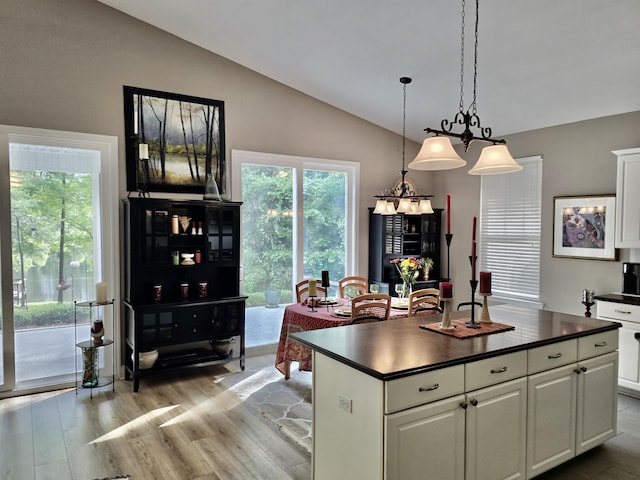 kitchen featuring white cabinets, lofted ceiling, light wood finished floors, dark countertops, and decorative light fixtures