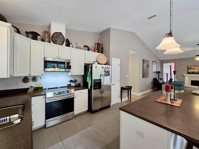 kitchen featuring dark countertops, hanging light fixtures, appliances with stainless steel finishes, open floor plan, and white cabinetry