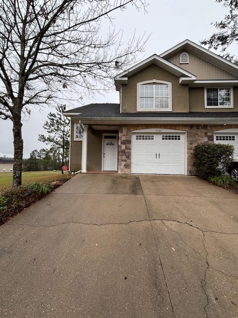 view of front facade featuring stone siding, an attached garage, concrete driveway, and stucco siding