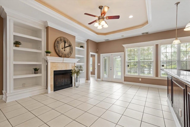 unfurnished living room featuring light tile patterned flooring, ornamental molding, ceiling fan, a tray ceiling, and built in features