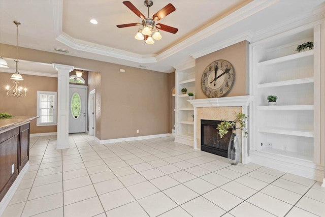 unfurnished living room featuring light tile patterned flooring, a tray ceiling, a premium fireplace, decorative columns, and built in features