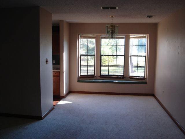 unfurnished room with carpet floors, a textured ceiling, and a chandelier