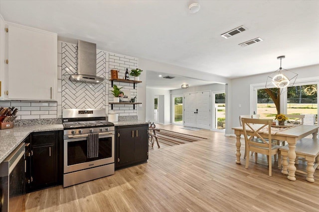 kitchen with wall chimney range hood, tasteful backsplash, light hardwood / wood-style floors, gas stove, and decorative light fixtures